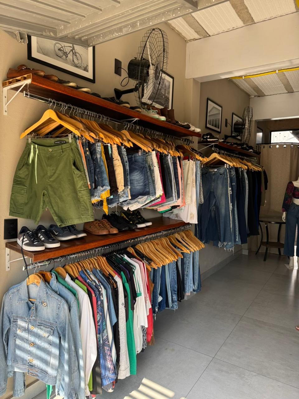 Estante com bolsas, acessórios e roupas dobradas no Brechó da Lola